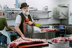 Un homme se tient devant un plan de travail en acier inoxydable avec un gros morceau de viande.