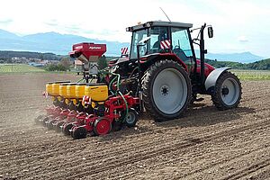 Un tracteur tire un semoir à soja dans un champ dont le sol a été fraîchement travaillé.