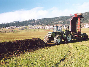 Un tracteur se trouve devant un endain de compost en plein champ avec une machine à retourner les endains