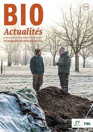 Page de couverture du Bioactualités 3|24: Deux hommes en pleine conversation se tiennent dans un champ, avec des arbres en arrière-plan et un tas de compost au premier plan.