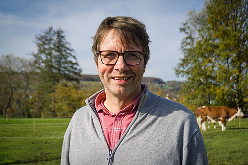 Un homme dans un pré avec une vache en arrière-plan.