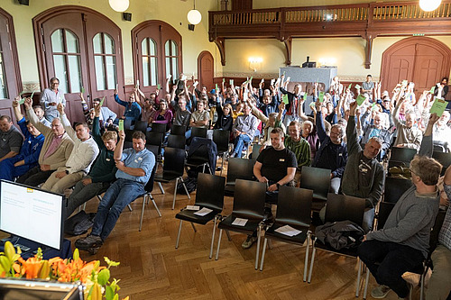Les membres de l'association pour la biodynamie sont assis dans une salle et lèvent leurs bulletins de vote.
