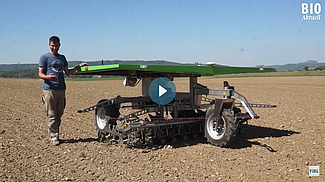Un jeune agriculteur marche à côté du robot dans le champ.