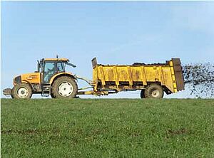 Tracteur et épandeuse à fumier au travail sur un champ.