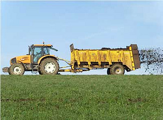 Tracteur et épandeuse à fumier au travail sur un champ.