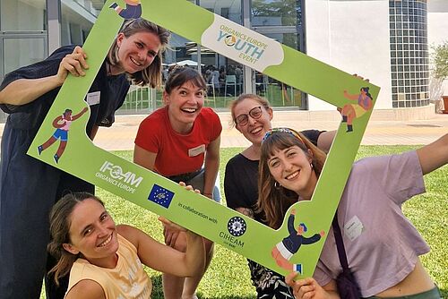 [Translate to Französisch:] Cinq jeunes femmes tiennent un grand cadre photo sur lequel est inscrit Organics Europe Youth Event et rient face à la caméra.