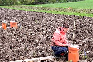 Une chercheuse accroupie dans un champ labouré avec des instruments de mesures