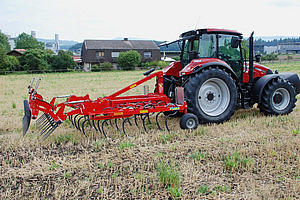 Une herse à dents à ressort attelée à un tracteur aère et ameublit le sol pour la préparation du lit de semence.