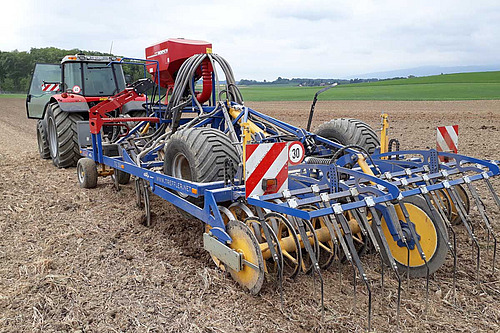 Tracteur avec machine bleue qui travaille le sol.