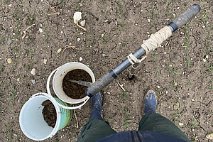 On aperçoit deux seaux remplis de terre depuis le haut. À côté se trouve une personne dont seuls les pieds sont visibles.