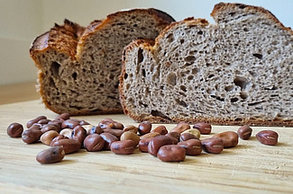 Sur une table se trouve une miche de pain entamée, devant laquelle sont disposées des graines de fèves. 