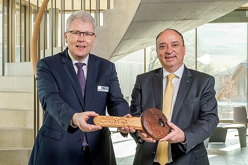 Deux hommes dans le nouveau bâtiment du FiBL tenant ensembles un clef en bois.