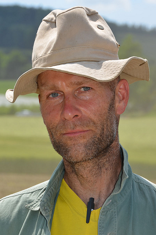 Tracteur et sarcleuse en train de sarcler un très jeune maïs.
Vue aérienne de la 2ème journée nationale des grandes cultures bio.
Portrait de Philippe Tavel.
Portrait de Bernard et Thierry Candaux
Des visiteurs se penchent sur le sol fraîchement