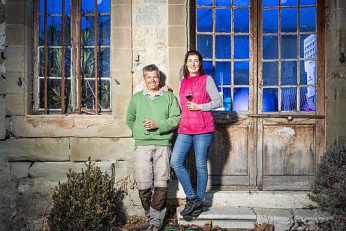 Un homme et une femme devant un bâtiment, un verre de vin rouge à la main.