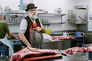 Un homme se tient devant un plan de travail en acier inoxydable avec un gros morceau de viande.