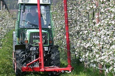 un appareil rouge à fils devant une rangée de pommiers avant fleur