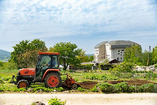 Tracteur travaillant un champ, à l'arrière-plan les bâtiments du Goetheanum.
