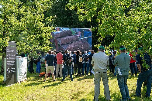 Des visiteurs  entre des arbres en regardant des échantillons de bêches 