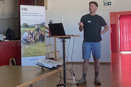 Un homme en short et t-shirt fait un exposé dans une salle.