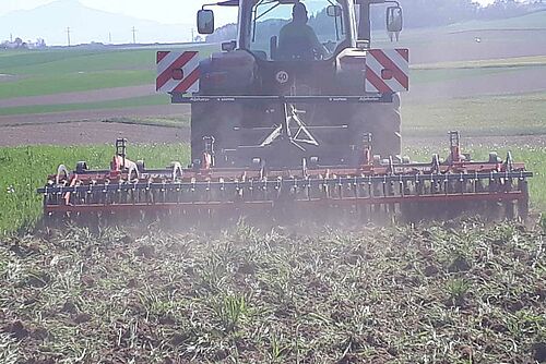 Tracteur avec machine rouge qui travaille le sol avec des pattes d'oie.