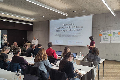Salle de conférence avec des auditeurs suivant une présentation sur la paludiculture.