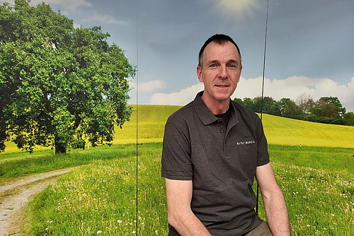 Portrait d'un homme sur fond de paysage verdoyant.