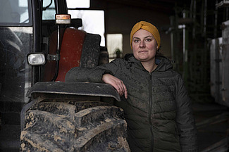 Une jeune femme est adossée à un tracteur, le bras posé contre celui-ci.