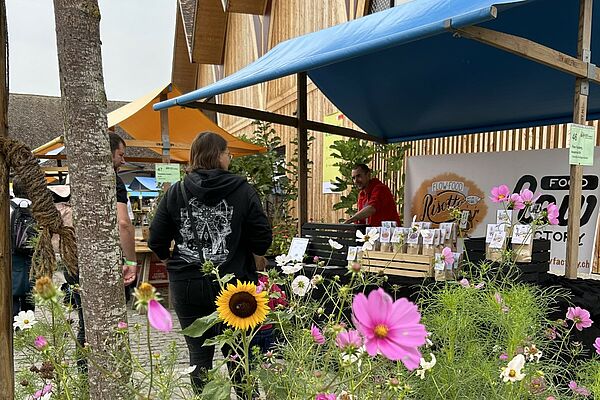 Impression du marché de la diversité avec des fleurs au premier plan, stand de marché à l'arrière-plan.