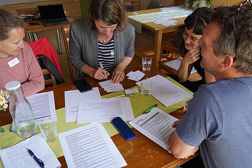 Quatre personnes sont assises à une table, penchées sur des papiers, une personne écrit quelque chose.