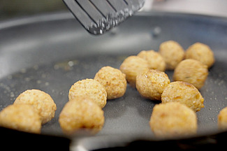 Dans une poêle, de petites boulettes dorées et croustillantes mijotent. On aperçoit encore une spatule. 
