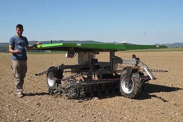 Un jeune agriculteur marche à côté du robot dans le champ.