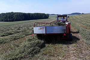 Petite machine derrière un tracteur, qui retourne un endain de luzerne.