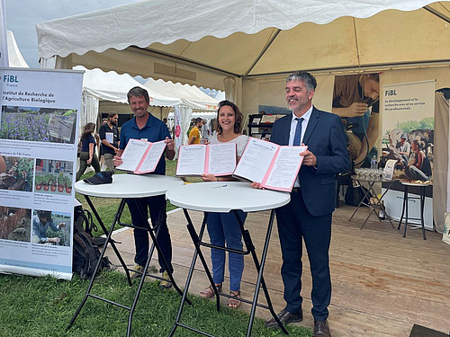 trois personnes tiennent chacune un contrat devant un stand.