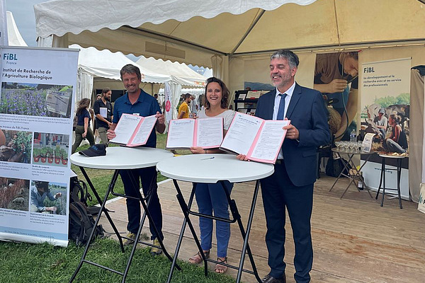 trois personnes tiennent chacune un contrat devant un stand.