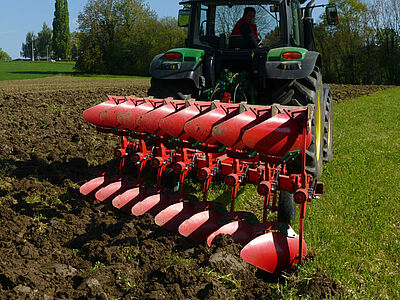 Charue rouge en plein ttravail dans une prairie.