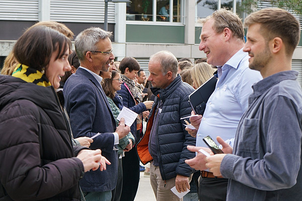 Zahlreiche Menschen stehen sich in zwei Reihen gegenüber und diskutieren.