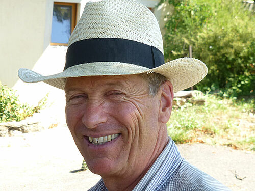 Portrait de Jean_Luc Tschabold souriant avec un chapeau de paille.
Baies bleu foncé d'aronia sur leur buisson.
Jean-Luc Tschabold en train d'observer un de ses poiriers. 