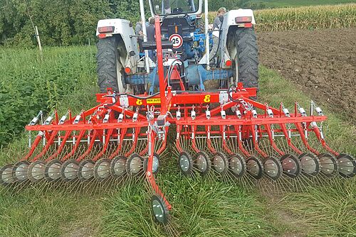 Sarcleuse rouge derrière un petit tracteur. 