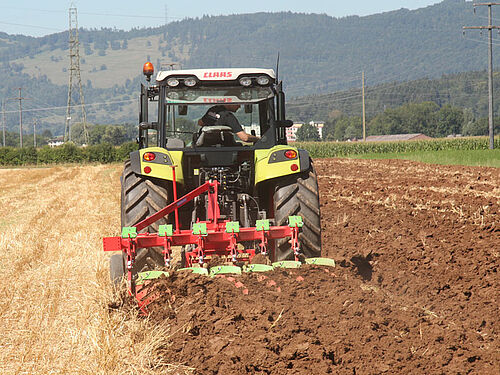 Tracteur tirant une charrue dans un champ de chaumes de céréales.