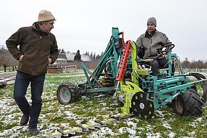 Deux hommes s'occupent d'un engin à hauteur d'homme dans une prairie. 