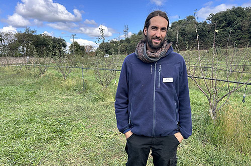 un jeune homme posé dans un verger.