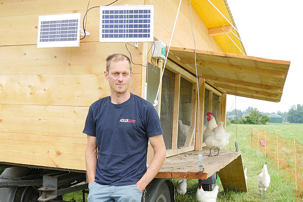 Un homme devant un poulailler mobile.