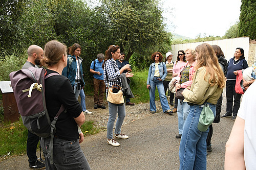 Un groupe de personnes est debout en cercle sur un chemin. Au milieu, une femme donne des explications. 