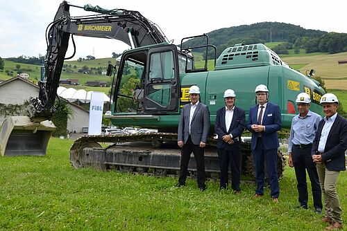 Cinq hommes devant un excavateur vert