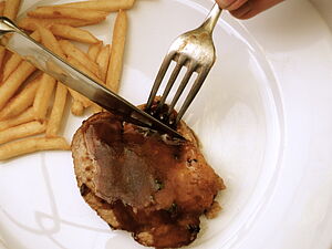  Une assiette de frites et un morceau de viande, une fourchette et un couteau coupent la viande.