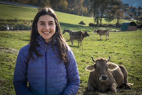 Une femme se tient dans un pré avec des vaches en arrière-plan.