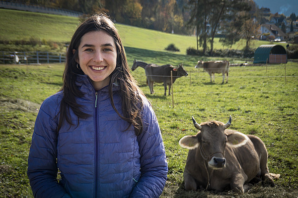 Une femme se tient dans un pré avec des vaches en arrière-plan.