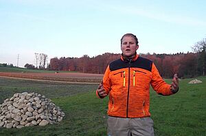 Un fermier se tient sur une prairie avec un tas de pierre pour les belettes