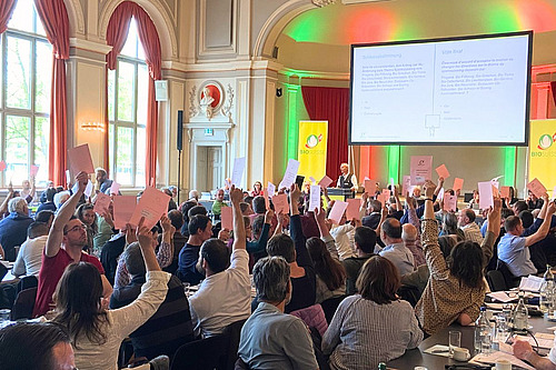 Abstimmung durch Handerheben in einem Saal mit rund hundert Personen.