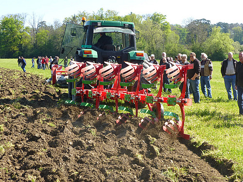 Tracteur et charrue en action dans un champ. Autour de la charrue, plusieurs agriculteurs observent la qualité du travail de la charrue